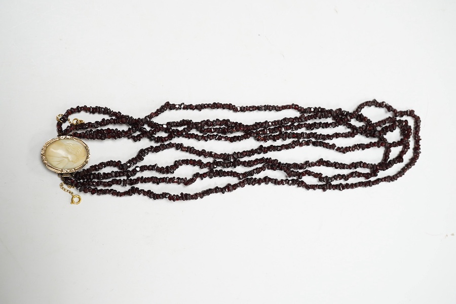 A late 19th/early 20th century multi strand rough cut garnet set necklace, with a yellow metal mounted oval cameo shell clasp, 43cm. Condition - poor to fair